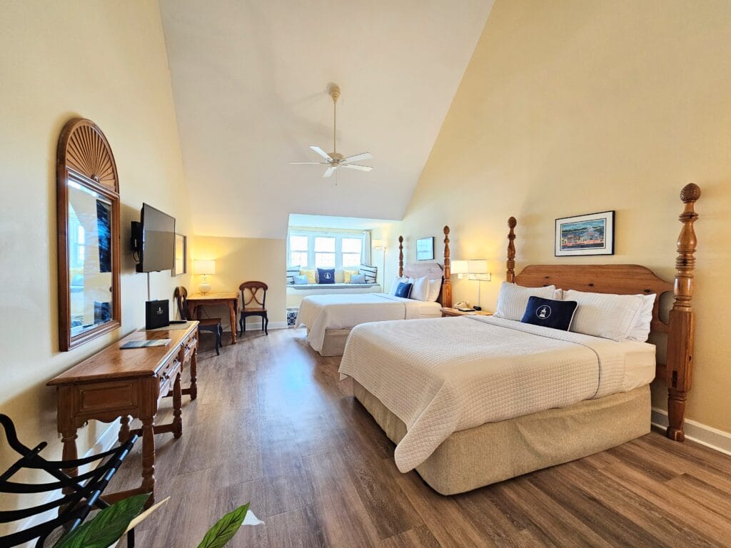 Interior view of a third floor room featuring two (2) queen beds, an alcove window seat, dining area for two, and mounted 43" flatscreen cable television at Inlet Inn.